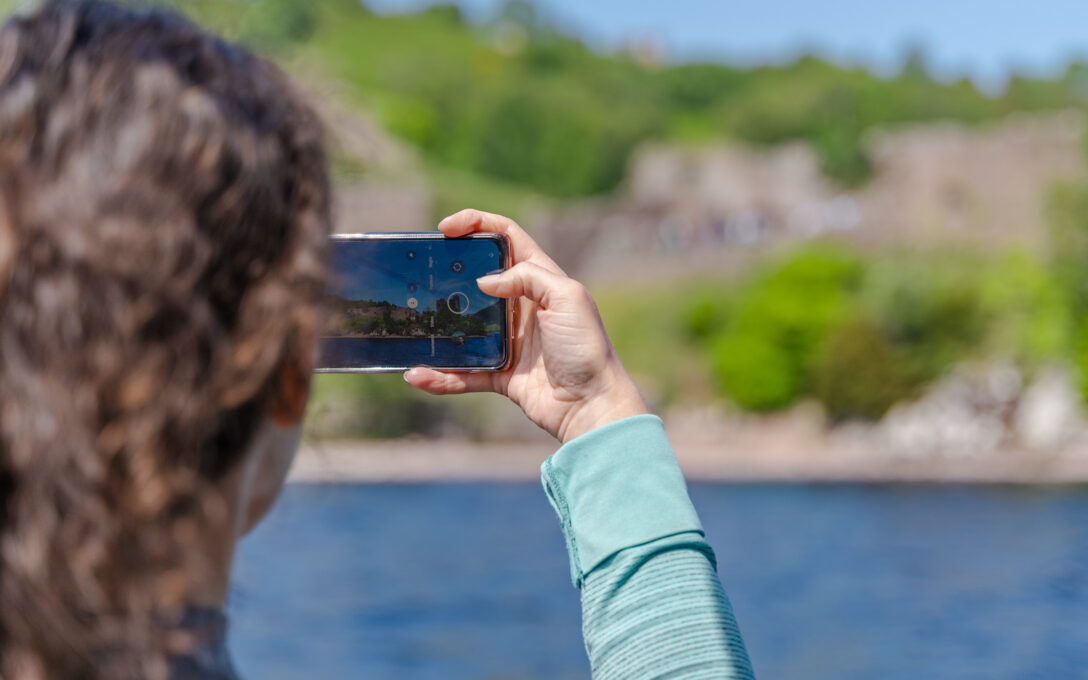 A woman takes a photo of Loch Ness on her phone.