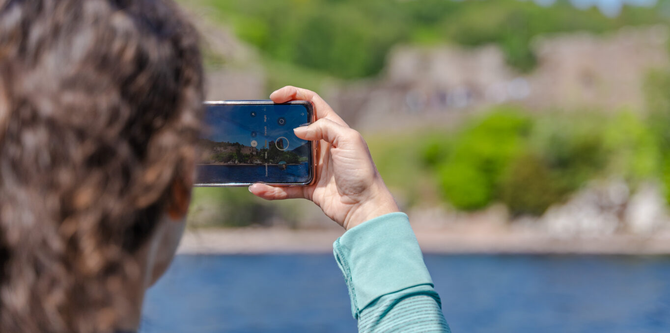 A woman takes a photo of Loch Ness on her phone.