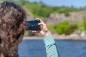 A woman takes a photo of Loch Ness on her phone. 
